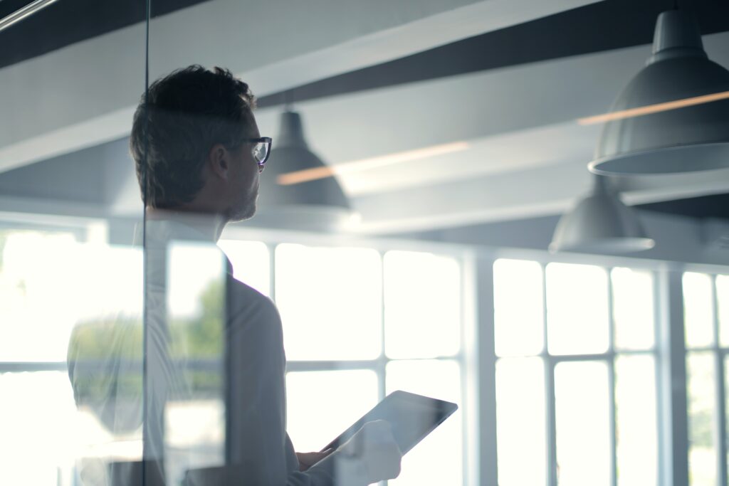 The view of a middle aged male business professional in a modern glass office seen through an interior window 