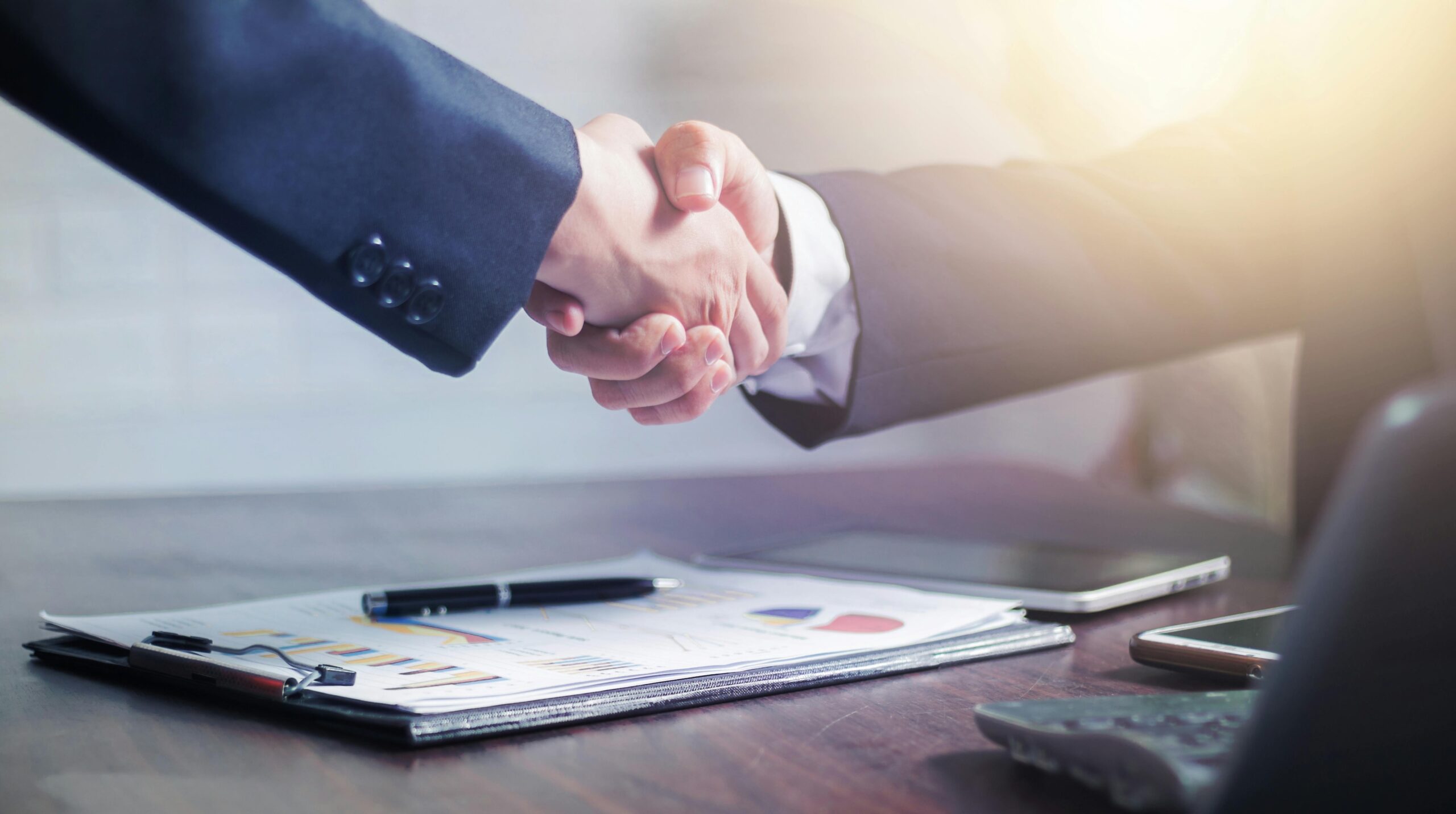 Two businessmen shown from the arms down wearing suits and shaking hands