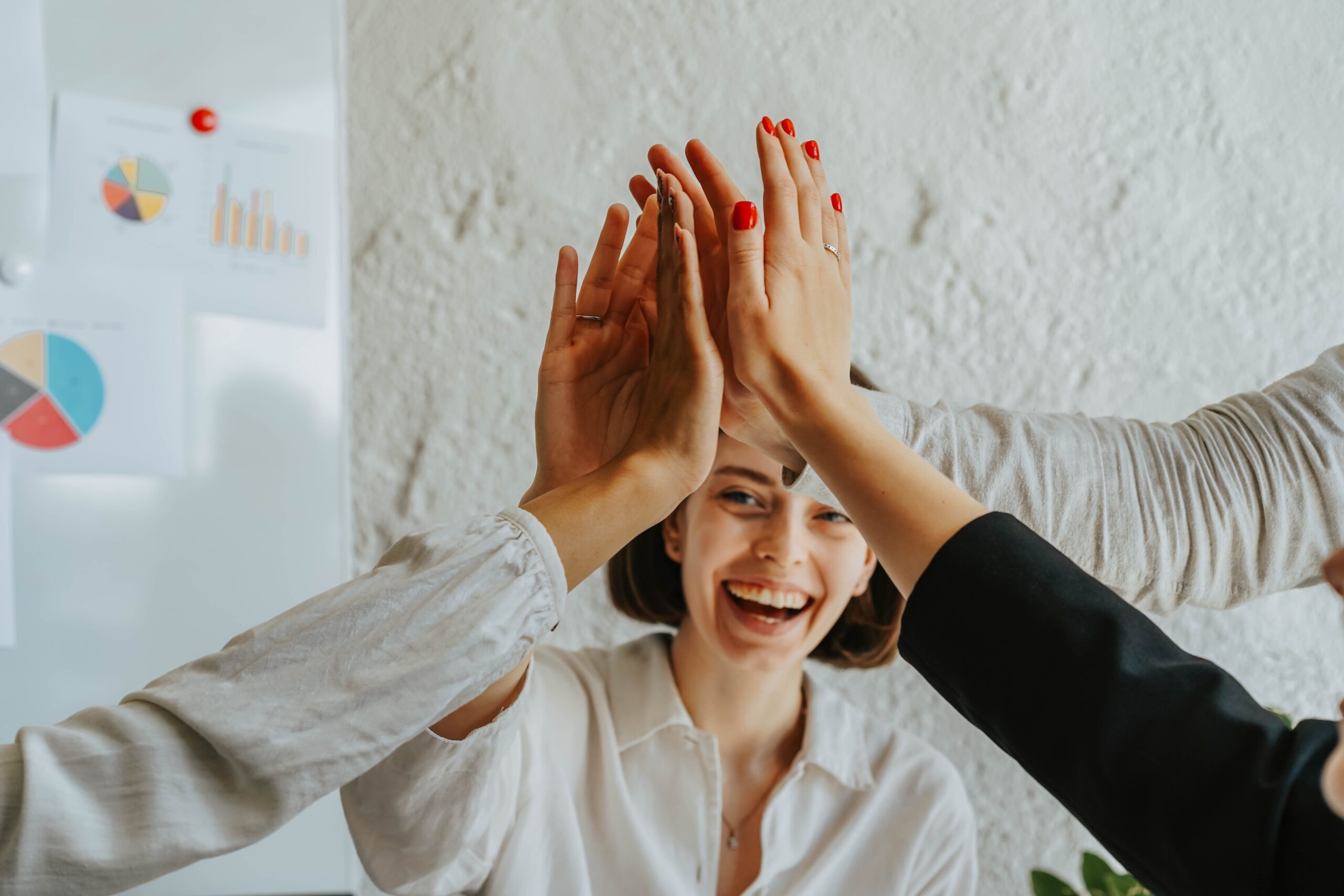 A group of young entrepreneurs brings theri hands together in celebration with one face of a young woman visible in the background