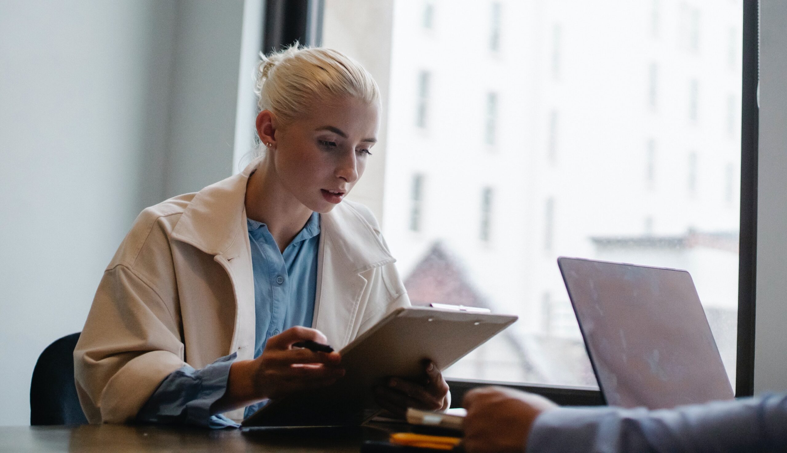 Young blonde woman analysing a tablet with an open laptop in front of her