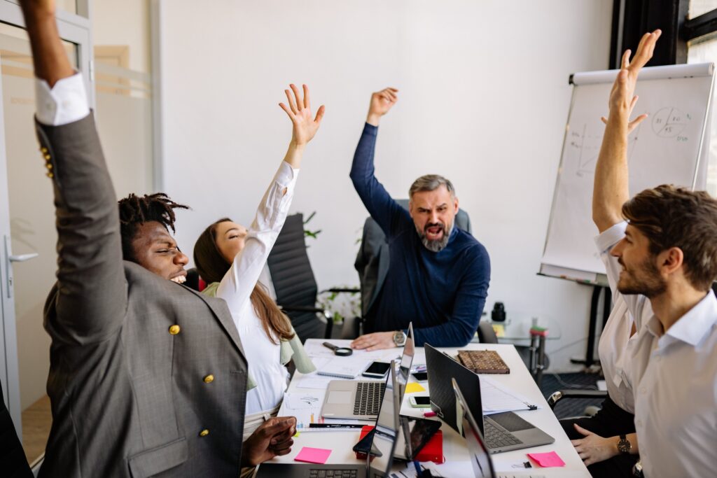 A table filled with laptops and four business professionals with their arm upraised celebrating a victory