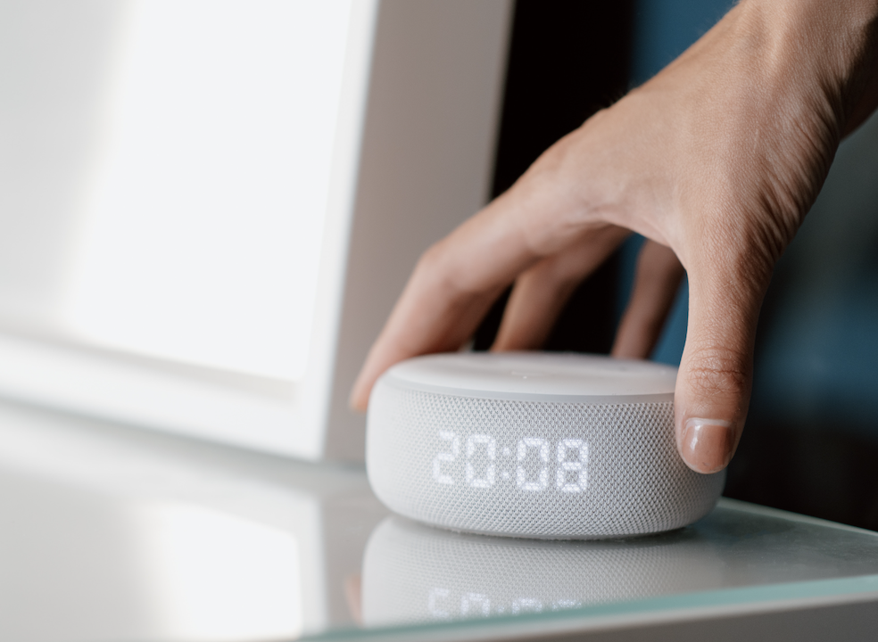 A single hand reaching out and touching a small, puck shaped Amazon smart home device