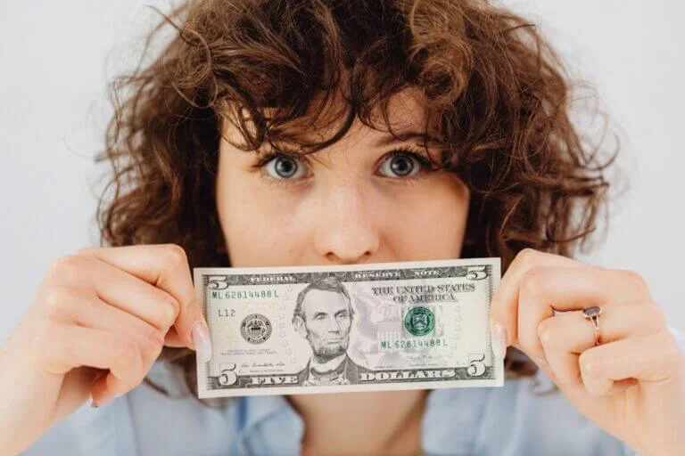 Woman holding 5 dollar bill in front of mouth